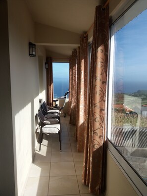 A balcony with a view of the sea, a chair, a table, and curtains. - House of Piety. (Piedade)