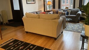 A living room with a beige sofa, a grey sofa, a patterned rug, and a window with a view of buildings.
