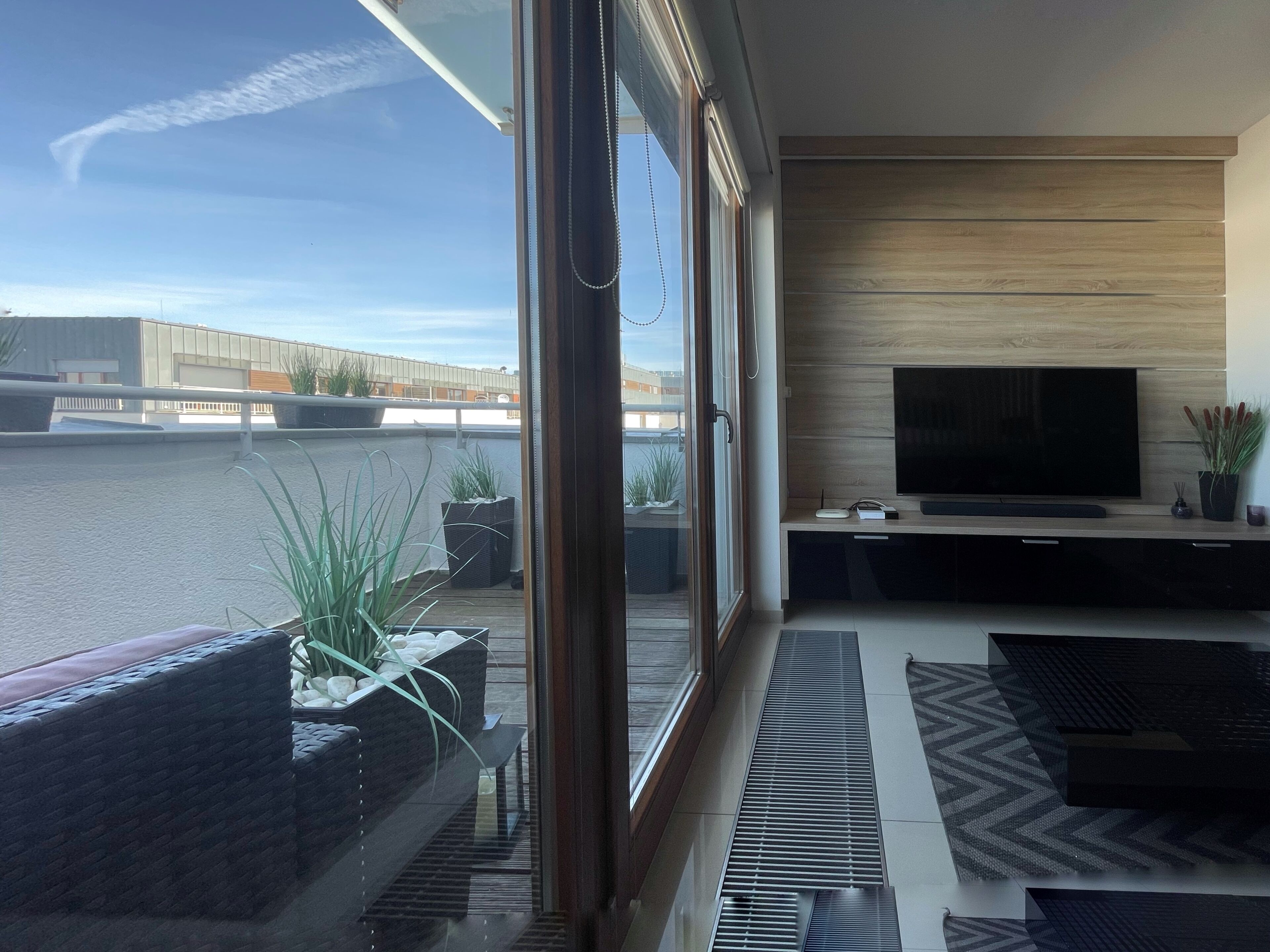 Una sala de estar moderna con un televisor grande, un ventanal corredero al exterior y vistas de un edificio.