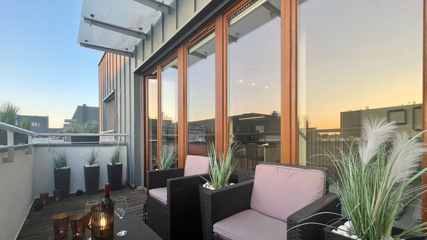 Une terrasse sur le toit, aménagée avec des meubles en osier, des plantes en pot et une rambarde en verre.