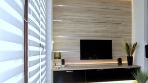 Un salon moderne avec un téléviseur à écran plat fixé à un mur en bois, une petite table avec une lampe et une plante en pot.