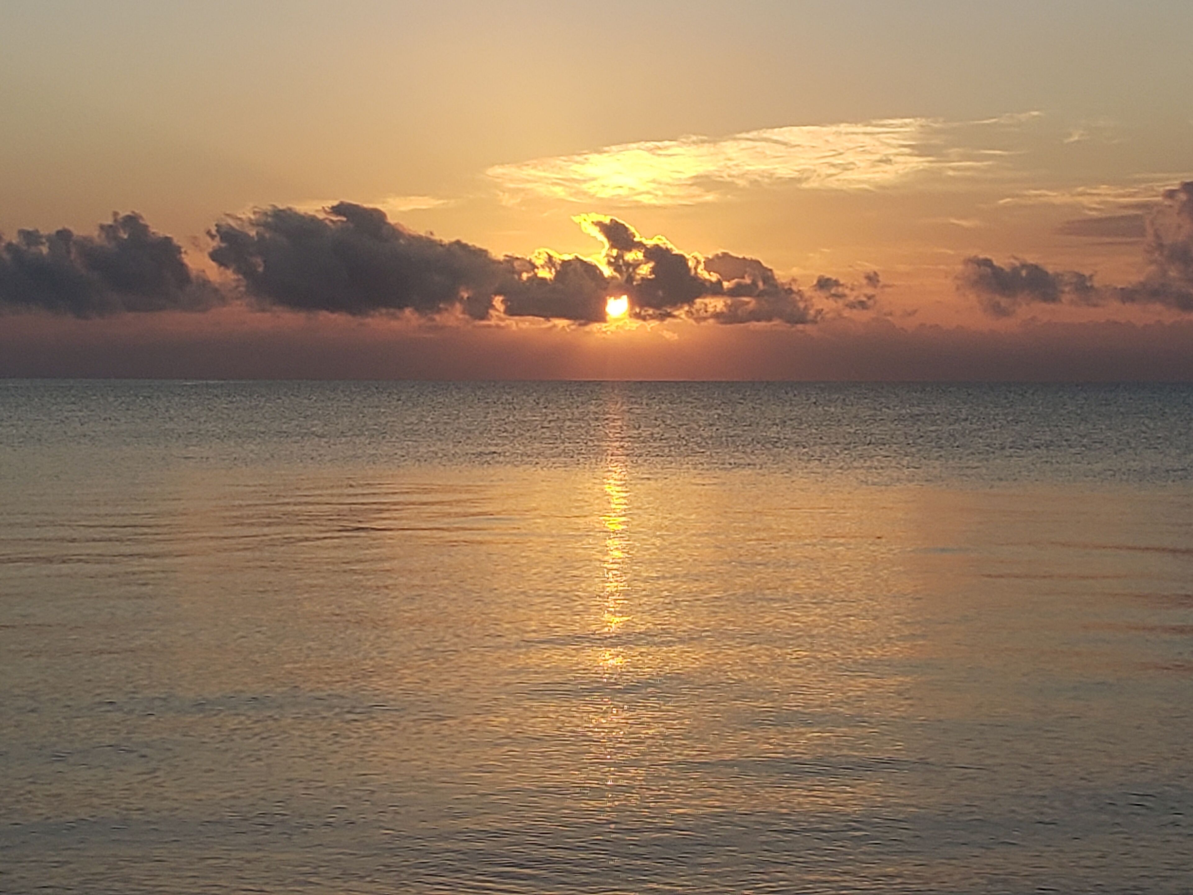 A sunset over a calm sea with clouds in the sky.
