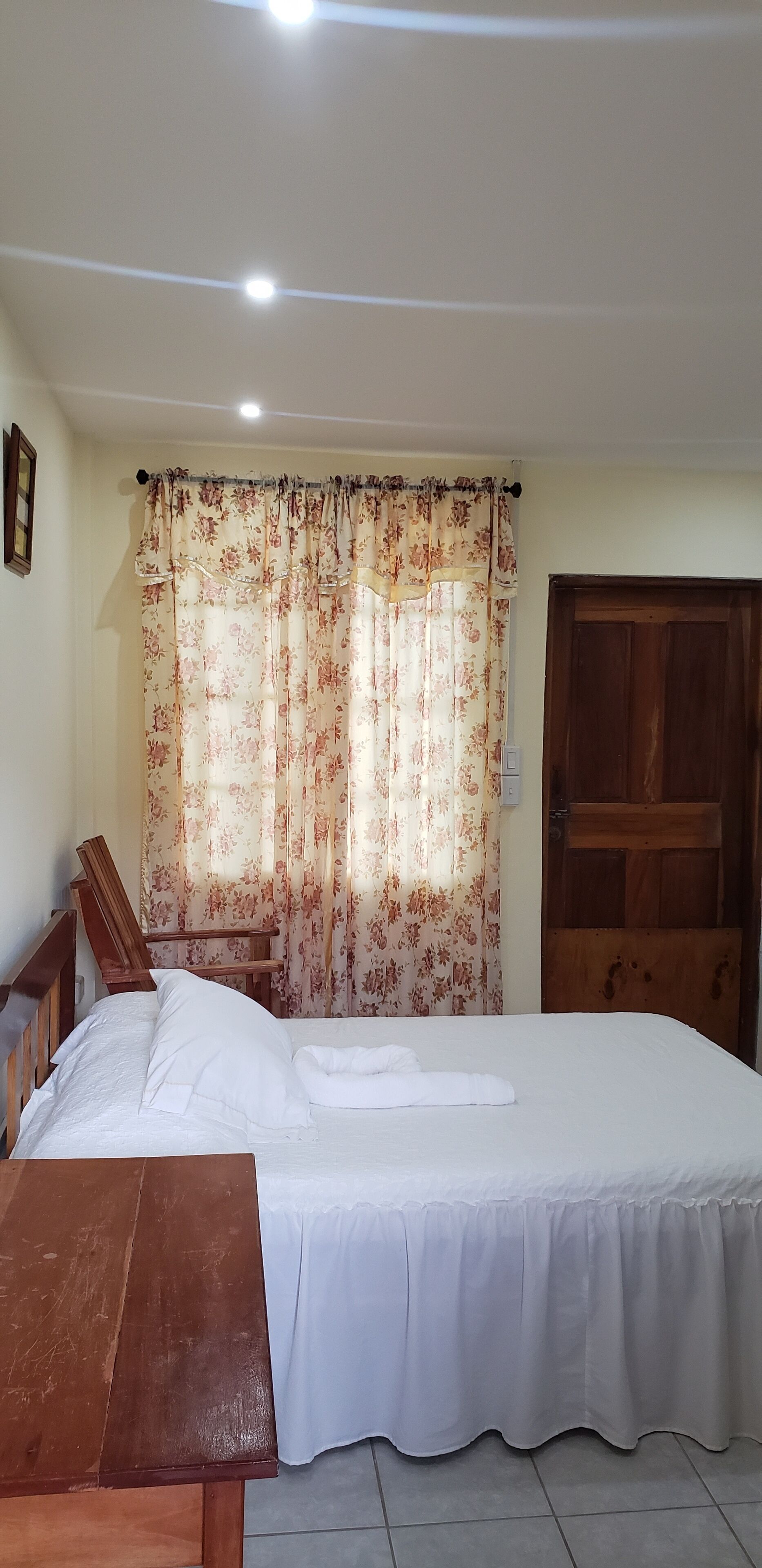 A bedroom with a bed, a wooden chair, a wooden door, and a curtain with a floral pattern.