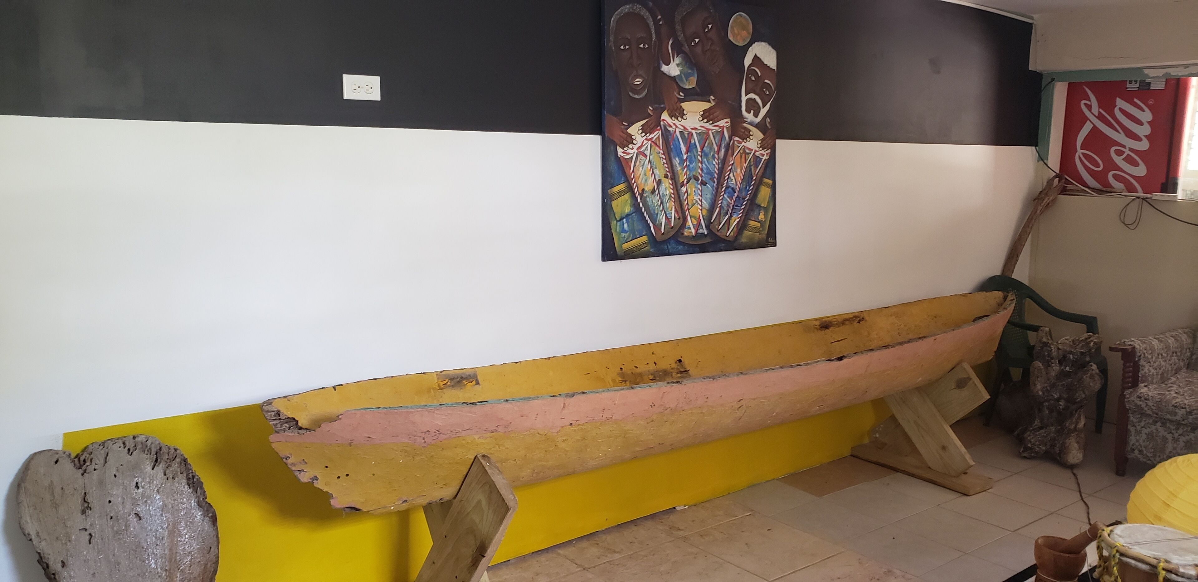 A room with a wooden bench, a wall-mounted painting, and a Coca-Cola sign.