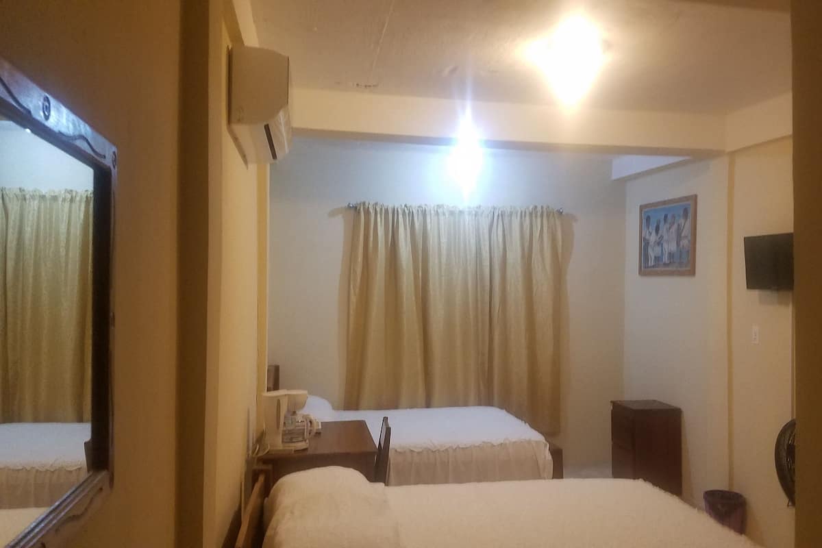 Habitación de hotel con dos camas, una mesita de noche con lámpara, un espejo, un cuadro en la pared y una cortina.