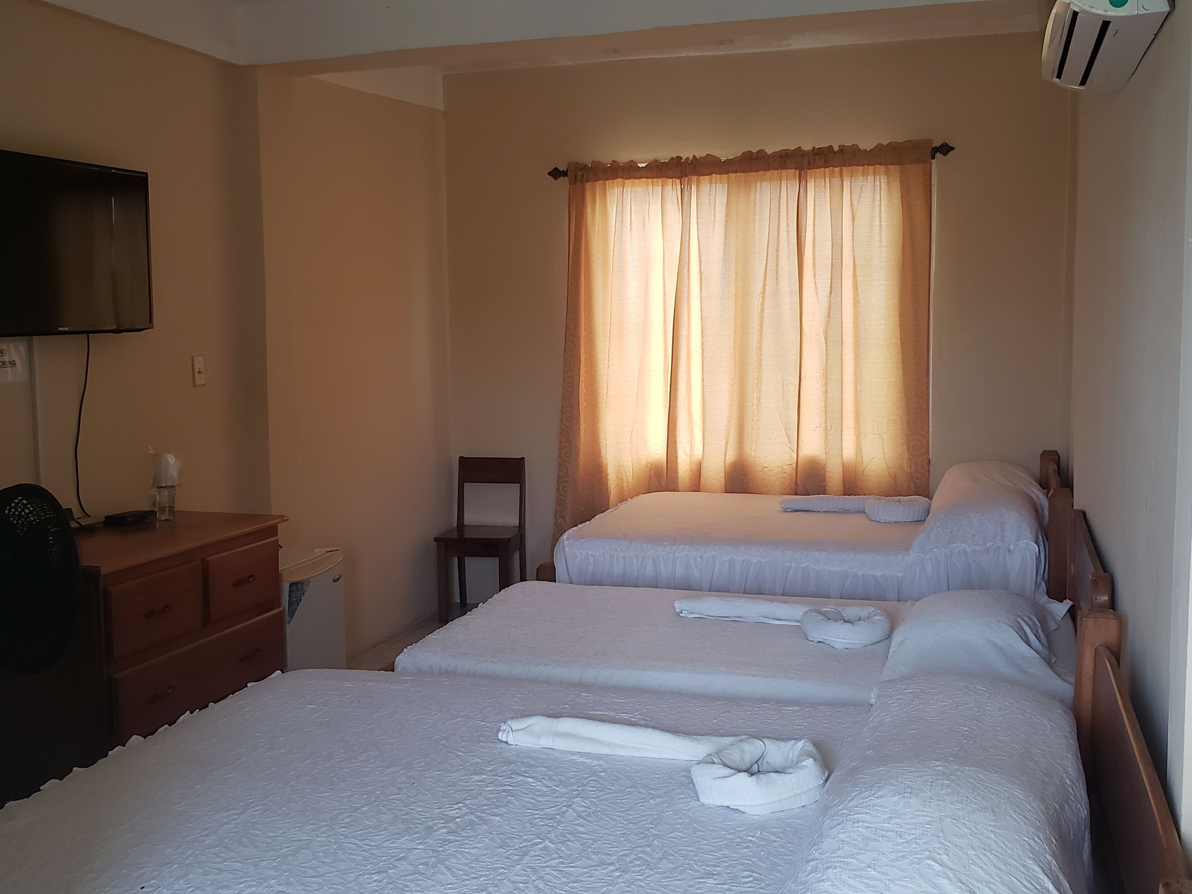 A hotel room with two beds, a wooden dresser, a chair, a television, and a window with curtains.