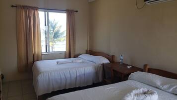 Habitación de hotel con dos camas, una mesita, una silla, una botella de agua y un televisor fijado a la pared.