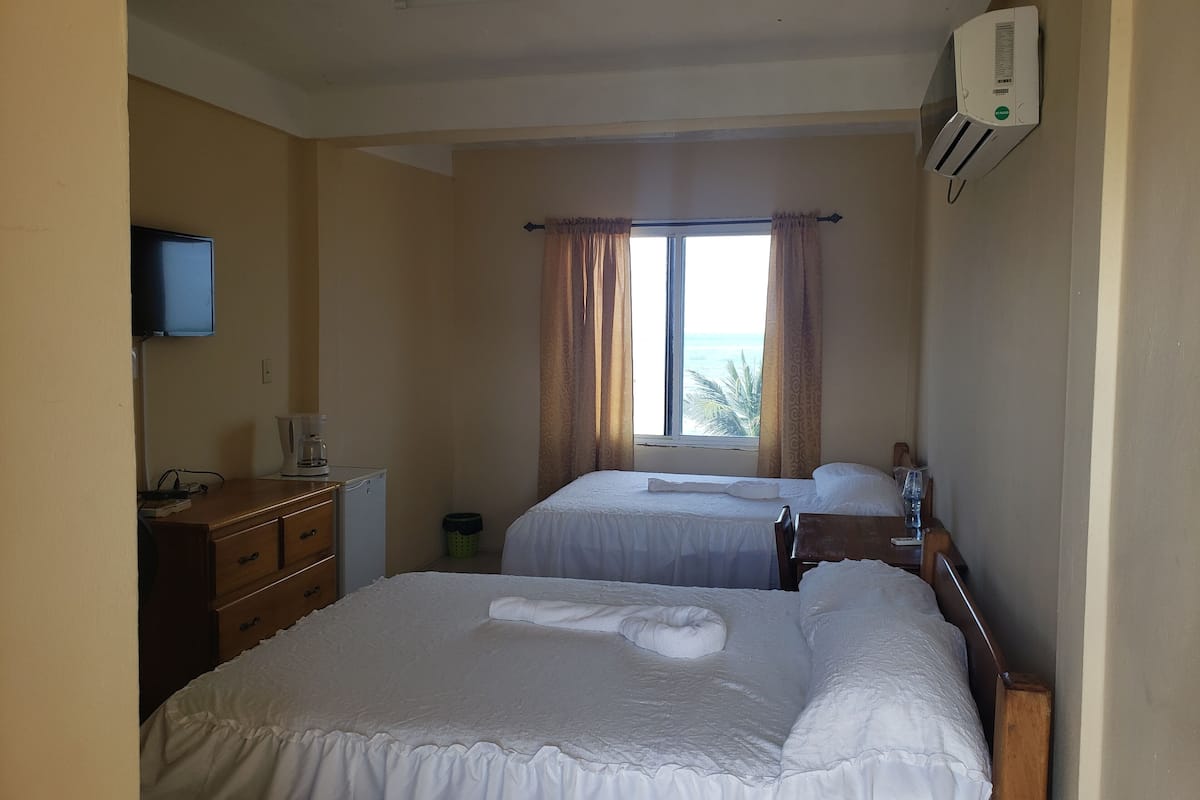 Habitación de hotel con dos camas, televisión, cafetera y ventana con cortinas.