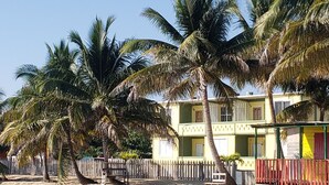 Una propiedad frente a la playa con un edificio de dos pisos, palmeras y una playa arenosa.
