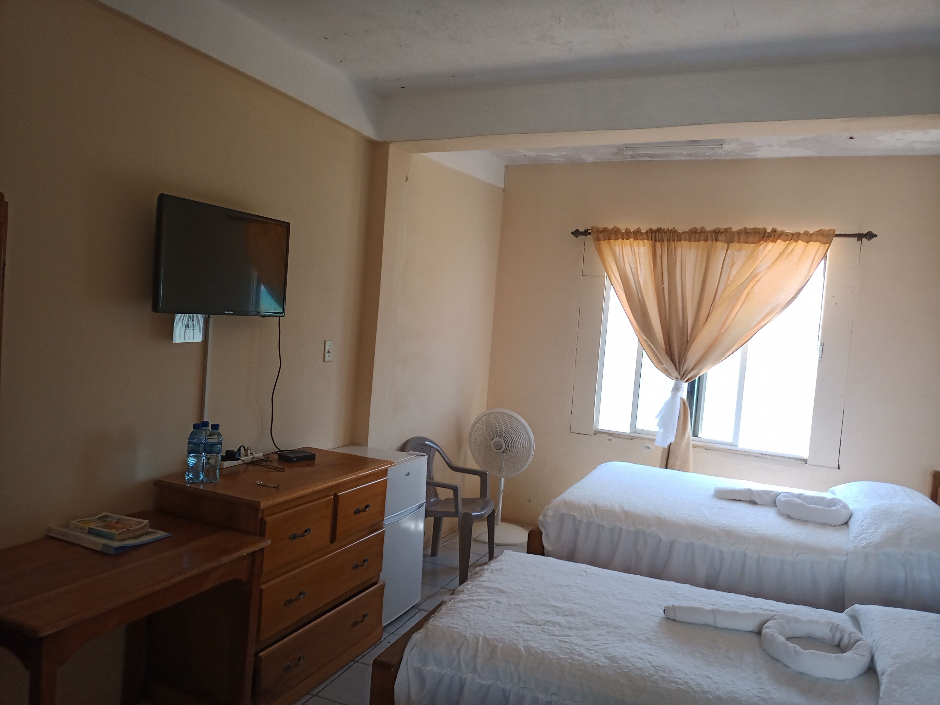 A hotel room with two beds, a desk with a television, a chair, and a window with curtains.