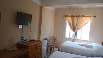 A hotel room with two beds, a desk with a television, a chair, and a window with curtains.