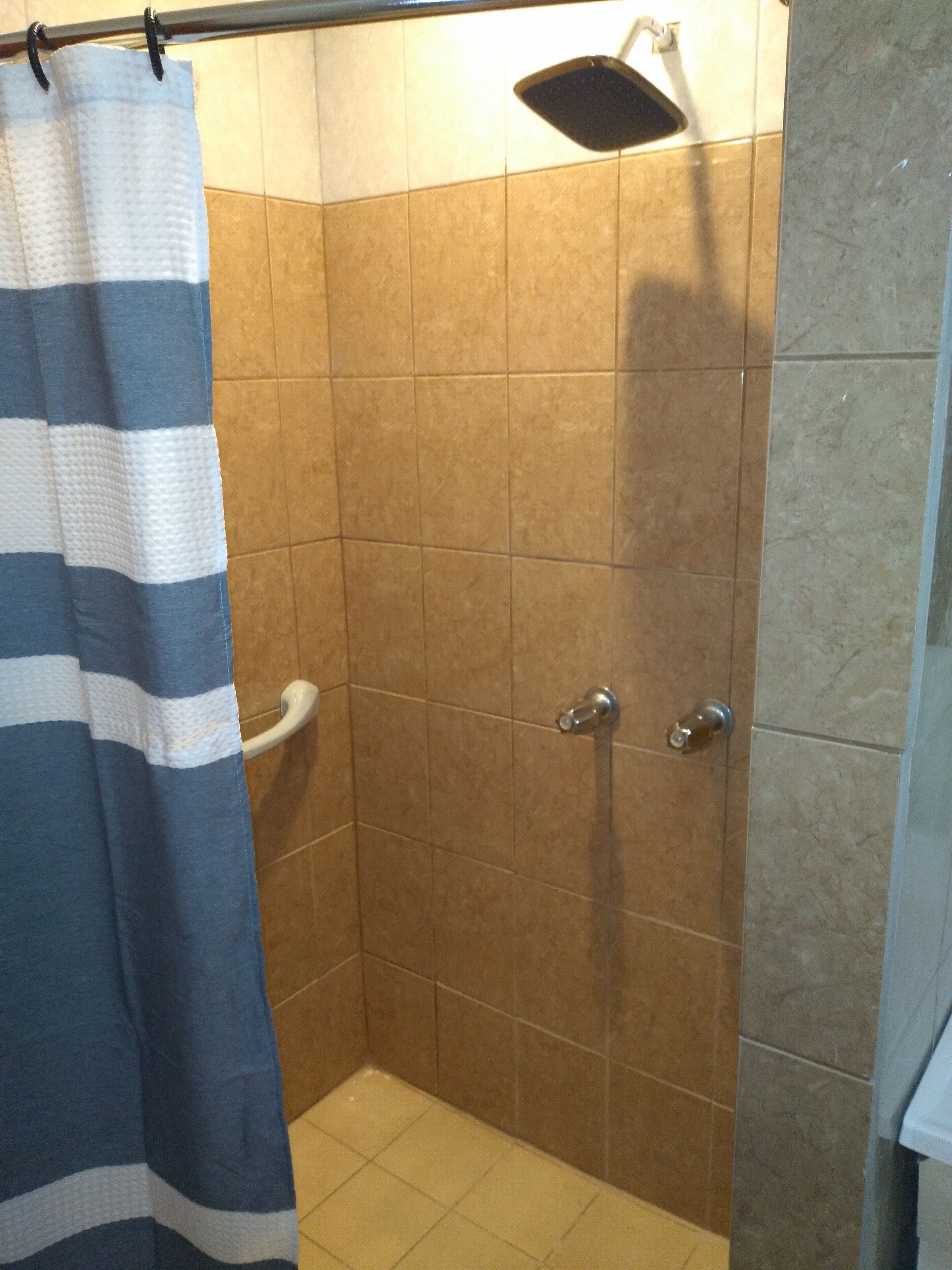 Un espace douche équipé d’un porte-serviettes, d’une pomme de douche et de murs carrelés.