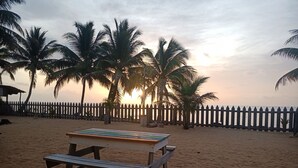 Una playa con una mesa y sillas de madera, palmeras y una valla de madera.