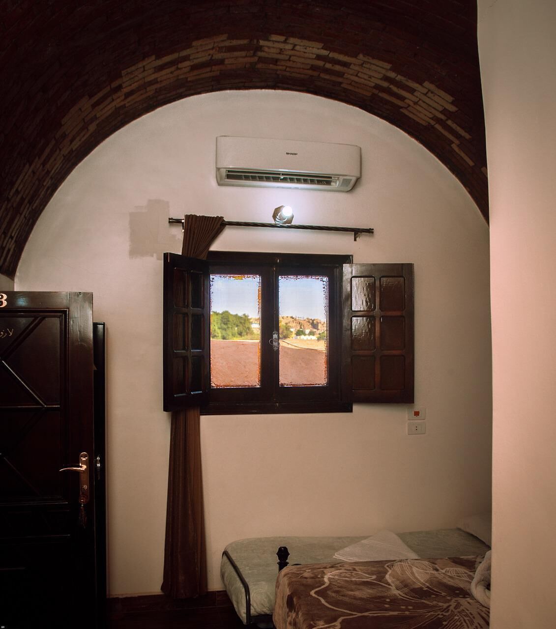 Ein Schlafzimmer mit Bett, Fenster mit Vorhängen, einer Klimaanlage und einer Tür.