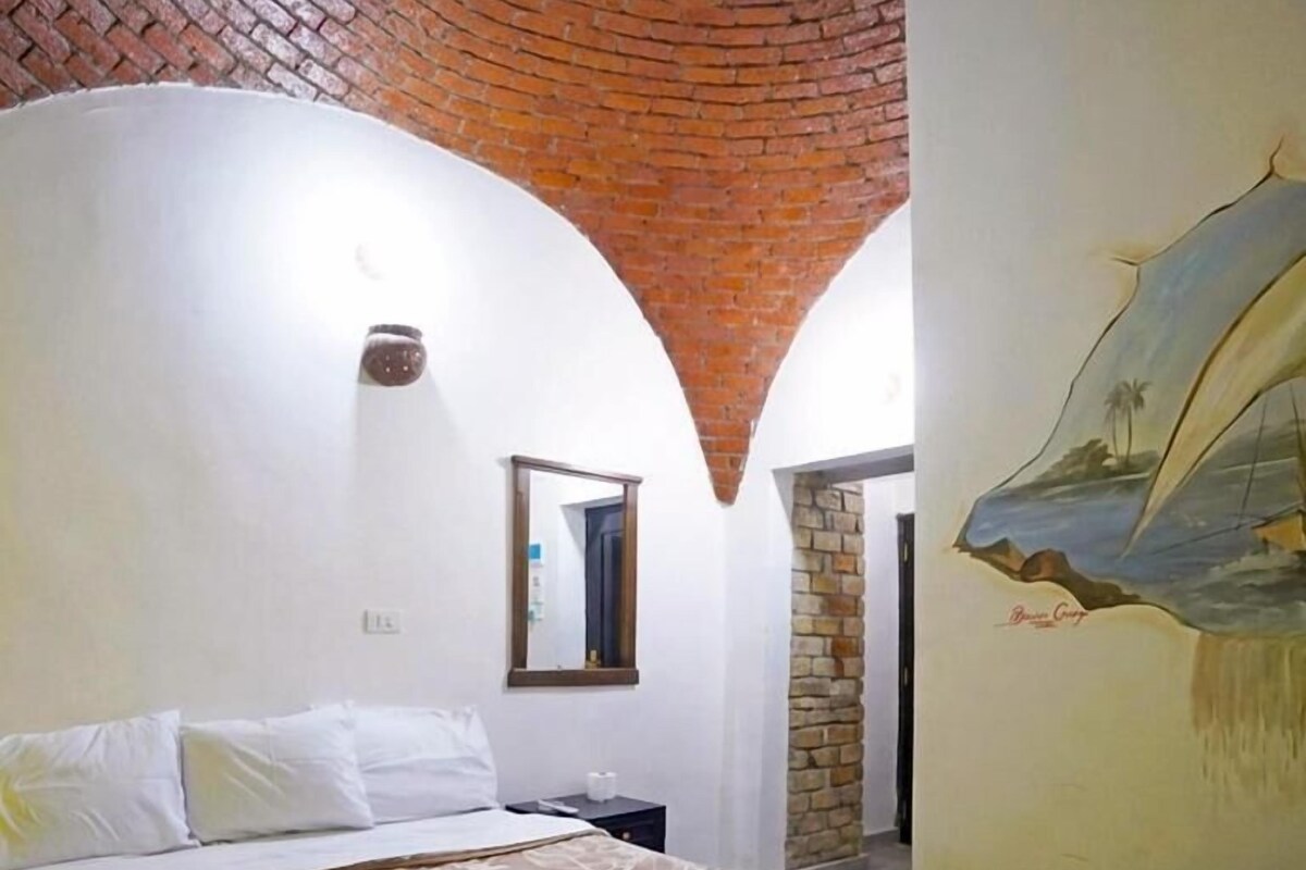 A hotel room with a bed, a brick wall, a mural, and a mirror.