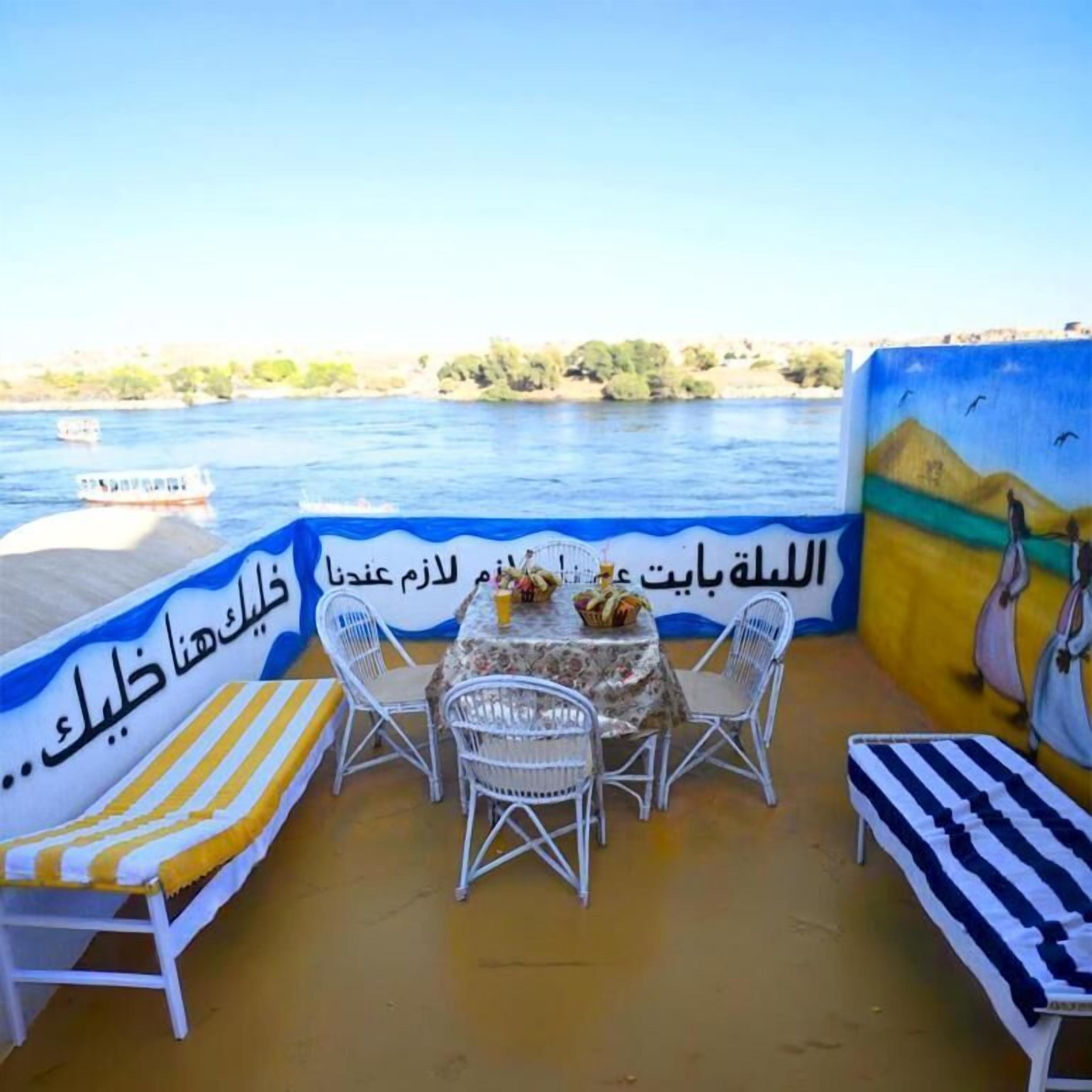 A terrace with a table and chairs, overlooking a river with boats.