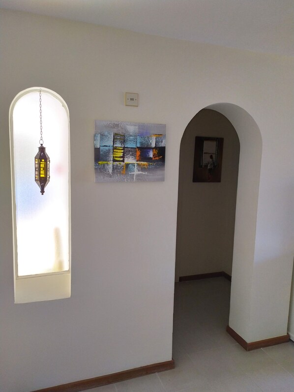 A hallway with a hanging lantern, a framed abstract painting, and a framed photograph on the wall. - Amazing ocean view apartment in Taurito, Mogán (Mogan)