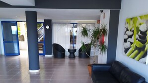 A spacious lobby with a blue sofa, two black chairs, a small table, and a potted plant. - Amazing ocean view apartment in Taurito, Mogán (Mogan)