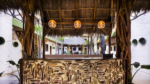 Un área de recepción con techo de paja, tallas de madera y luces esféricas colgantes.