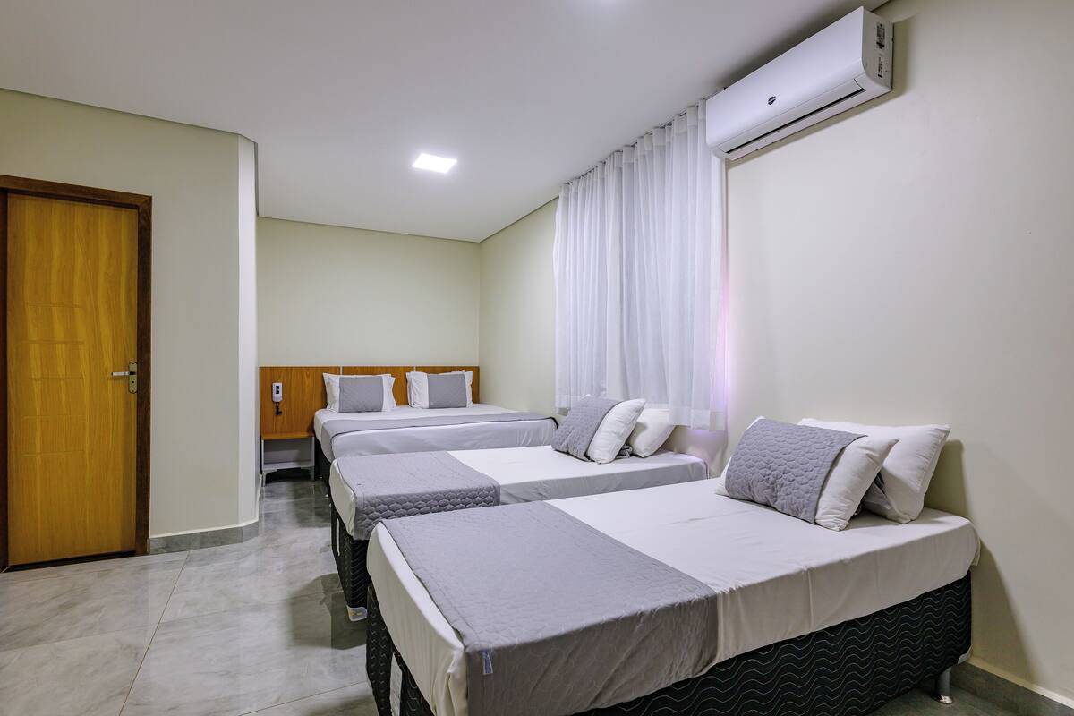 A hotel room with three beds, a wooden door, an air conditioning unit, and a tiled floor.