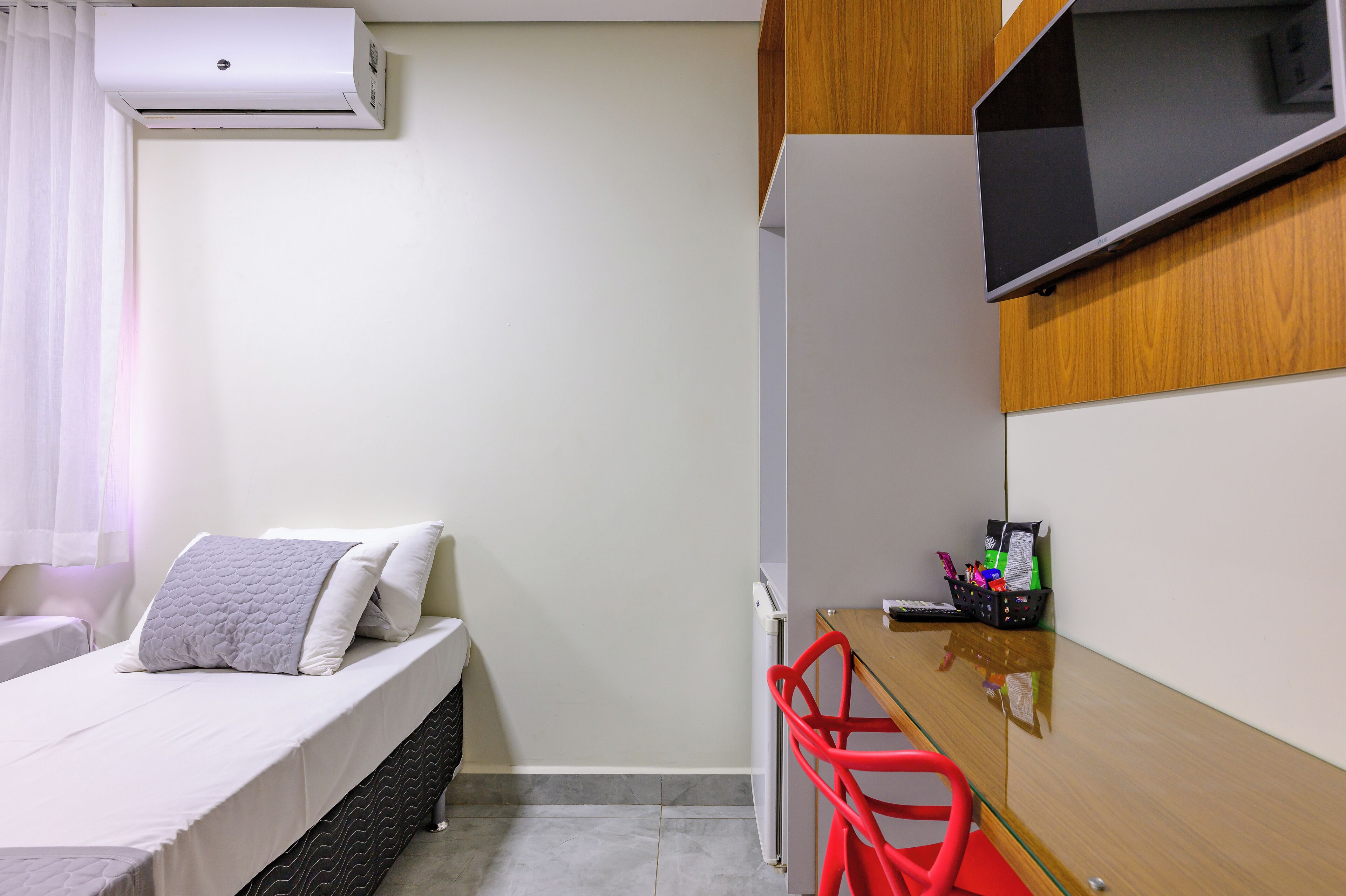 A compact room with a bed, a desk, a chair, a TV, and an air conditioner.