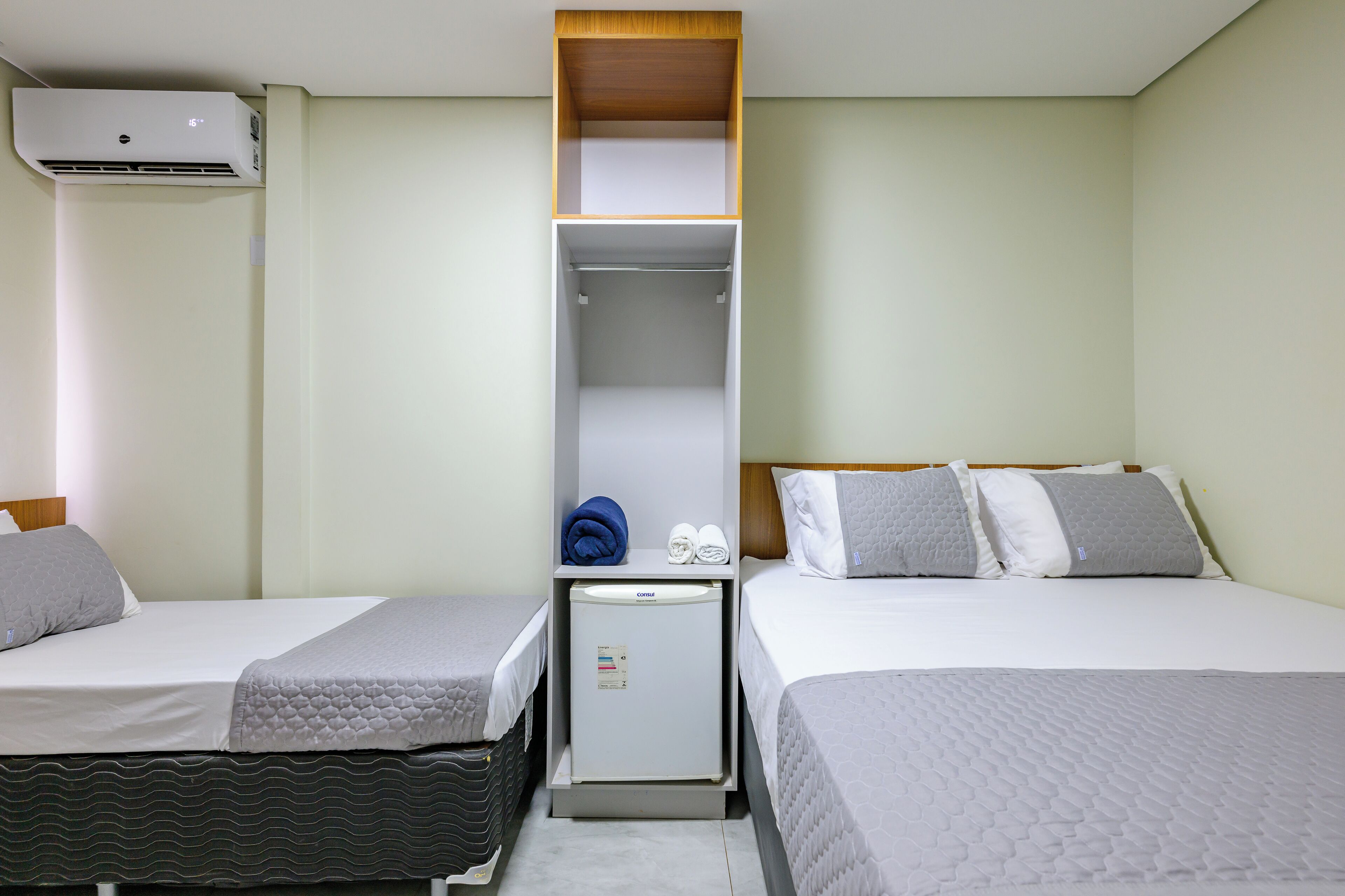 Habitación de hotel con dos camas, un refrigerador pequeño y un armario empotrado.