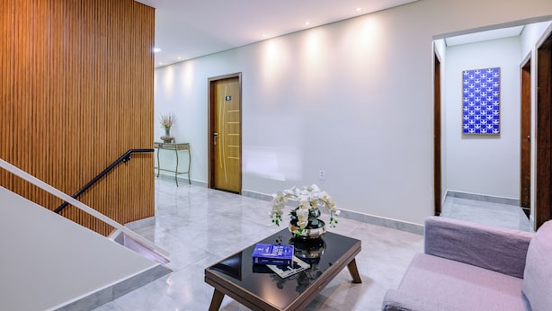 A modern lobby with a wooden panel wall, a glass coffee table with a vase and books, a plush armchair, and a door with a number sign. - OYO Hotel Brisa Tropical, Brasília (São Sebastião)