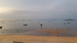 A beach with boats and a person in a red outfit. - OYO Pousada Encanto dos Anjos (Búzios)
