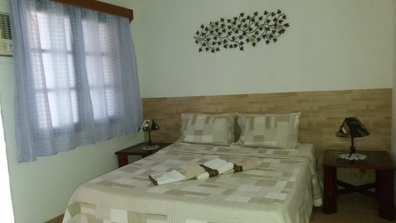 A bedroom with a bed, two nightstands, a wall-mounted lamp, and a decorative wall piece.