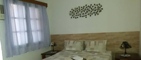 A bedroom with a bed, two nightstands, a wall-mounted lamp, and a decorative wall piece.