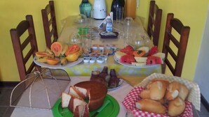 A table set with various food items including bread, pastries, and fruits, with chairs around the table. - OYO Pousada Encanto dos Anjos (Búzios)