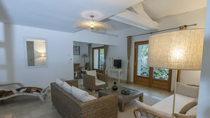 Ein geräumiges Wohnzimmer mit Korbmöbeln, einem Fernseher und einem großen Fenster mit Vorhängen.