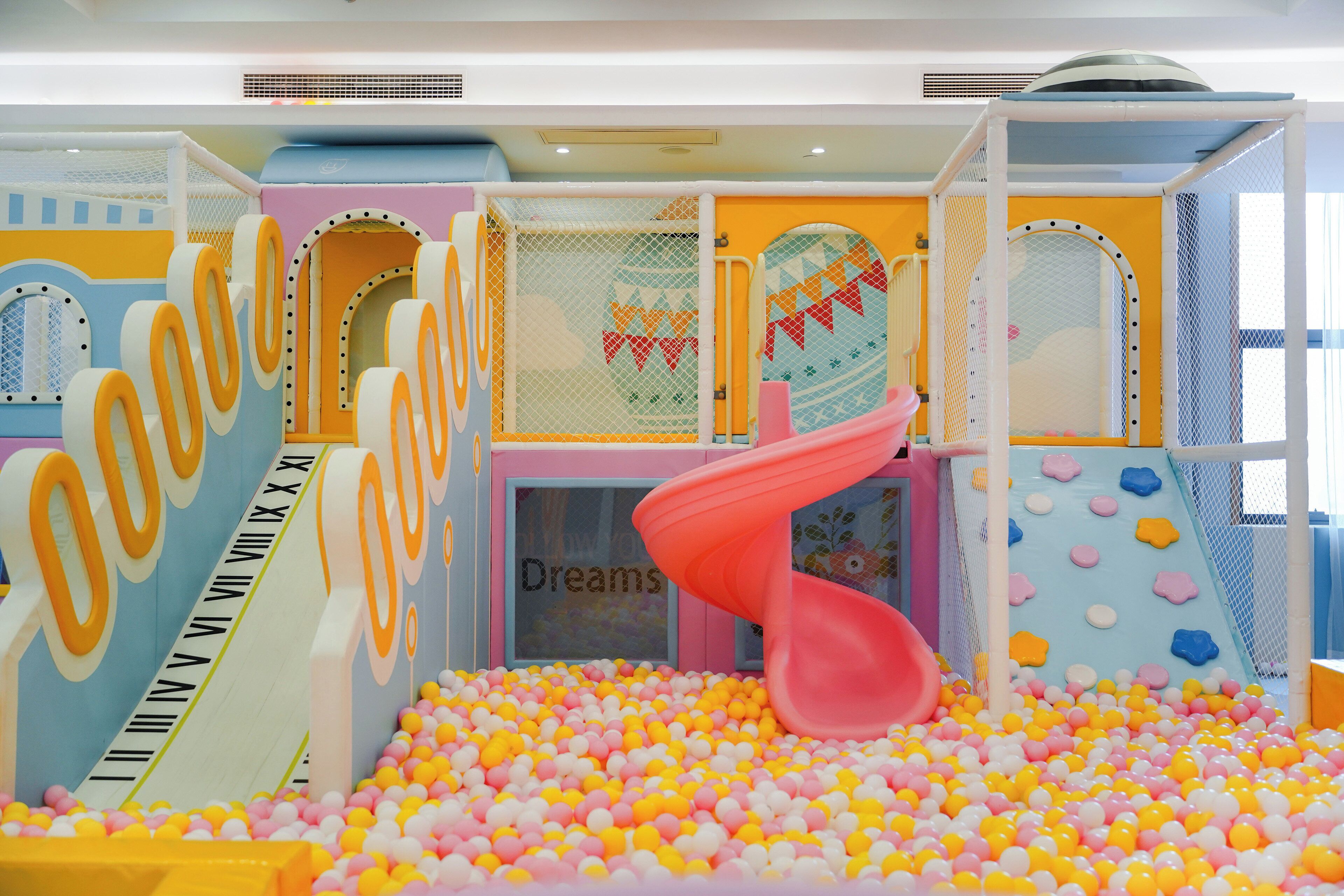 Un espace de jeux intérieur coloré, comprenant une piscine à balles, des toboggans et des structures de jeu.