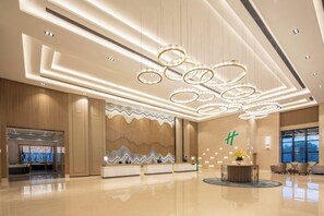 A modern hotel lobby with a reception desk, seating area, and a decorative ceiling with circular light fixtures.
