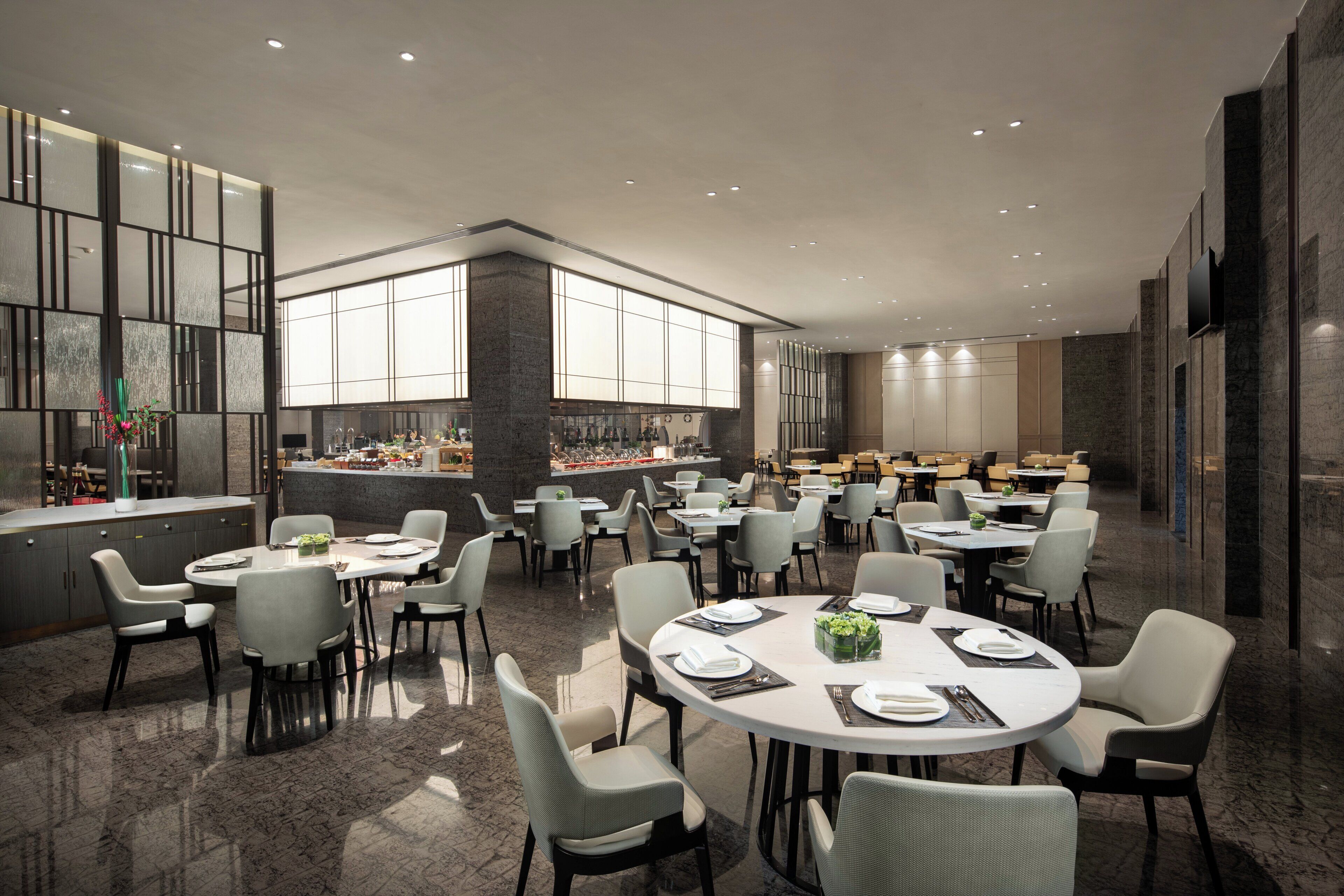 Een modern restaurant met ronde tafels en stoelen, een bar en grote ramen voor natuurlijk licht.