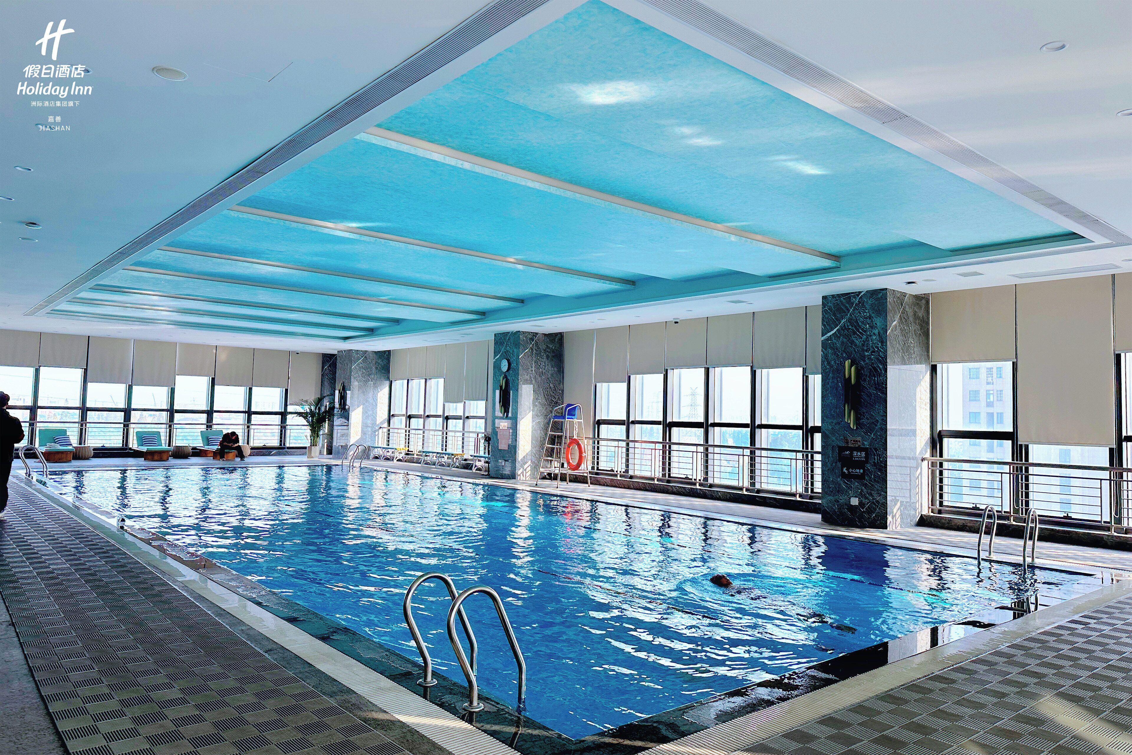 An indoor swimming pool with clear blue water, a tiled floor, and a ceiling with skylights.