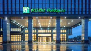 Entrada de un hotel Holiday Inn con fachada de vidrio, señalización iluminada y pavimento mojado.