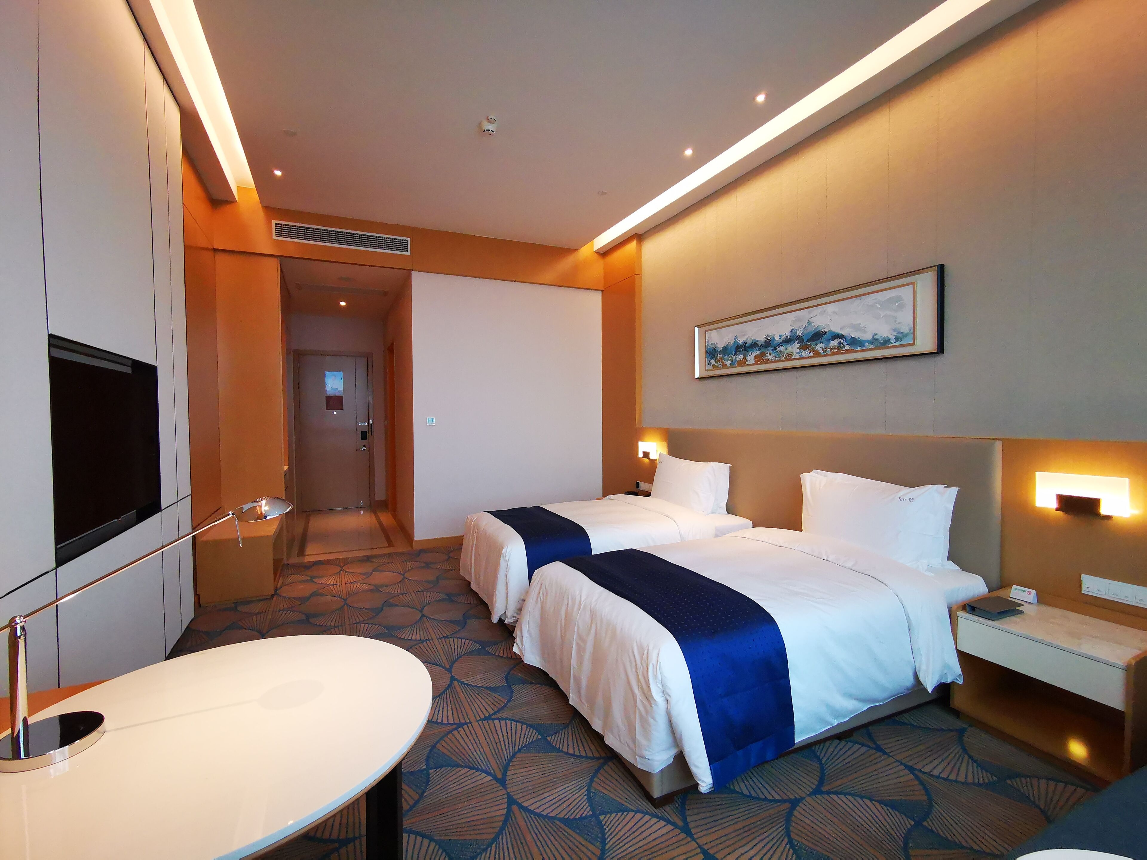 Habitación de hotel con dos camas, televisión, escritorio y un cuadro en la pared.