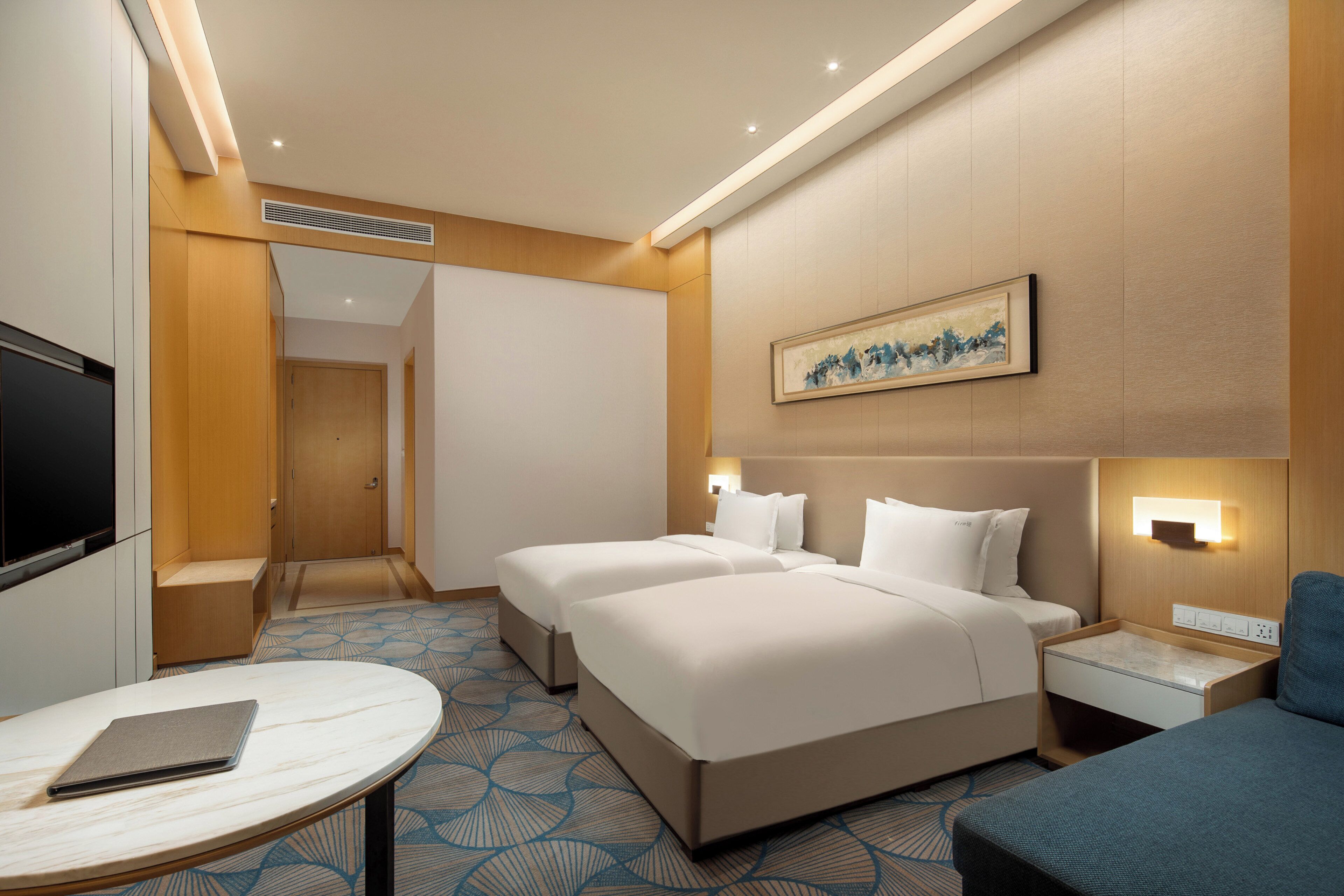 A hotel room with two beds, a desk, a TV, and a painting on the wall.