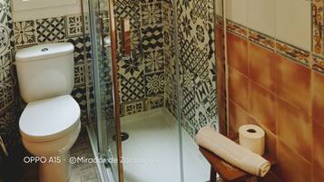 A bathroom with patterned tiles, a glass-enclosed shower, a toilet, and a towel rack.