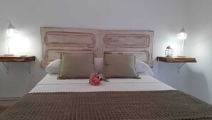 Un lit bien fait, recouvert d’une couverture marron, avec deux oreillers et une fleur rose. Deux tables de chevet, chacune surmontée d’une lampe, se trouvent de part et d’autre du lit.