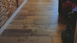 Une pièce avec un mur en briques, un plancher en bois, un canapé, une table à manger avec des chaises et une fenêtre avec des rideaux.