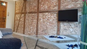 Une pièce avec un mur en briques, un téléviseur fixé au mur et une table en verre sur laquelle sont éparpillés divers objets.