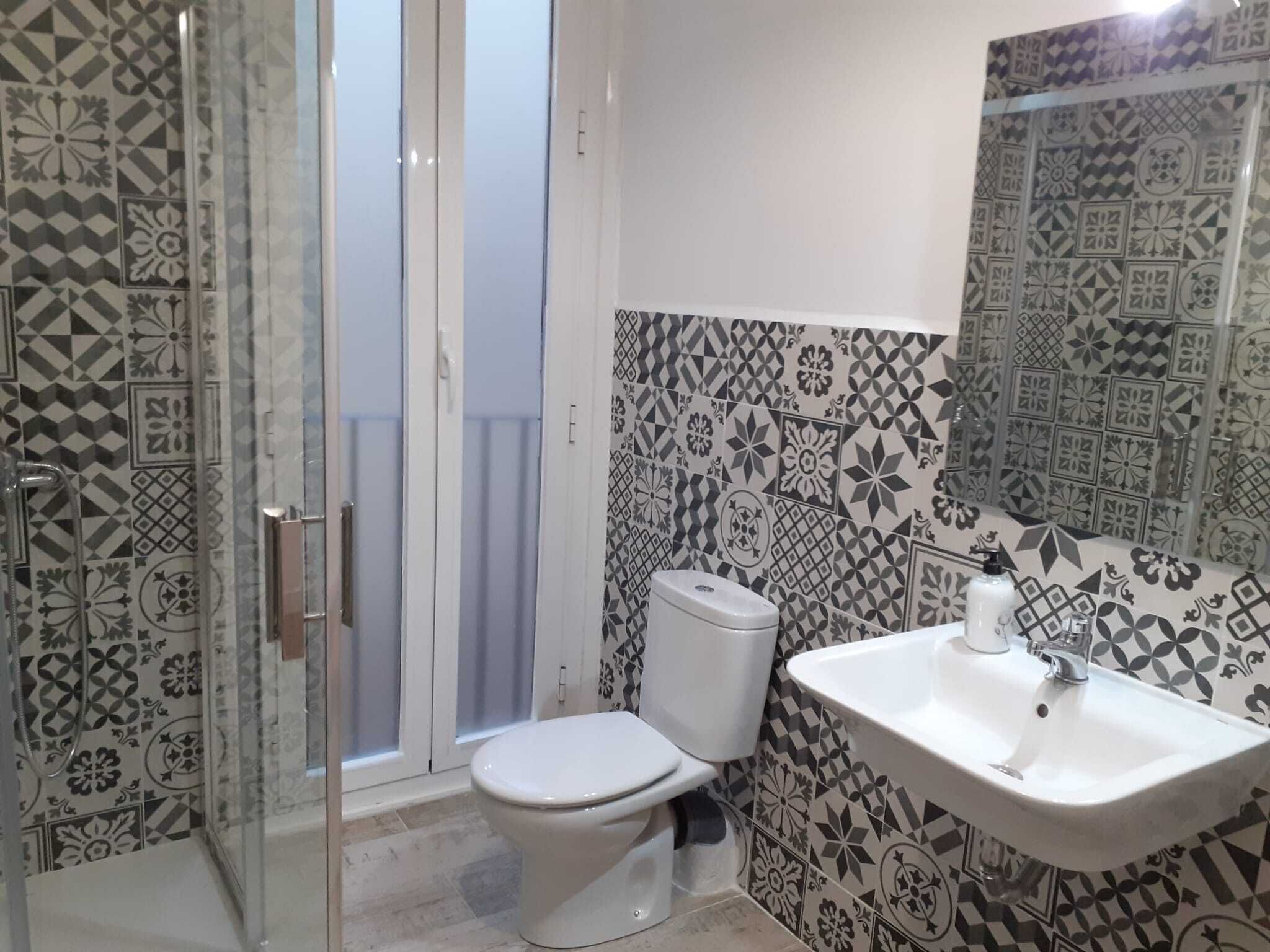 Ein Badezimmer mit gemusterten Fliesen, einer Toilette, einem Waschbecken und einer Duschkabine aus Glas.