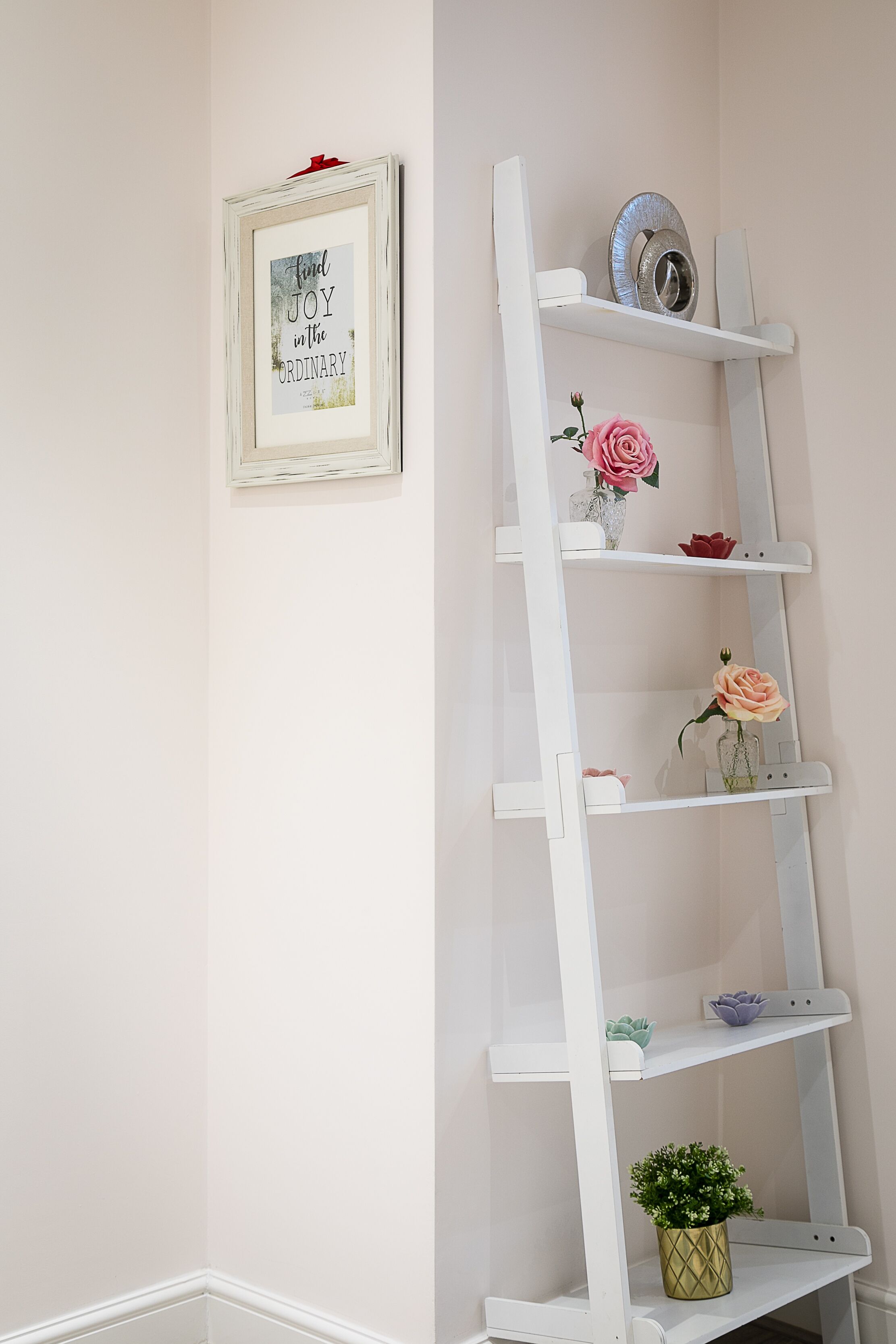 A white ladder shelf with decorative items and a framed quote on the wall.