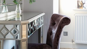 Une pièce avec un miroir, un vase de fleurs, une chaise et des œuvres d’art encadrées accrochées au mur.