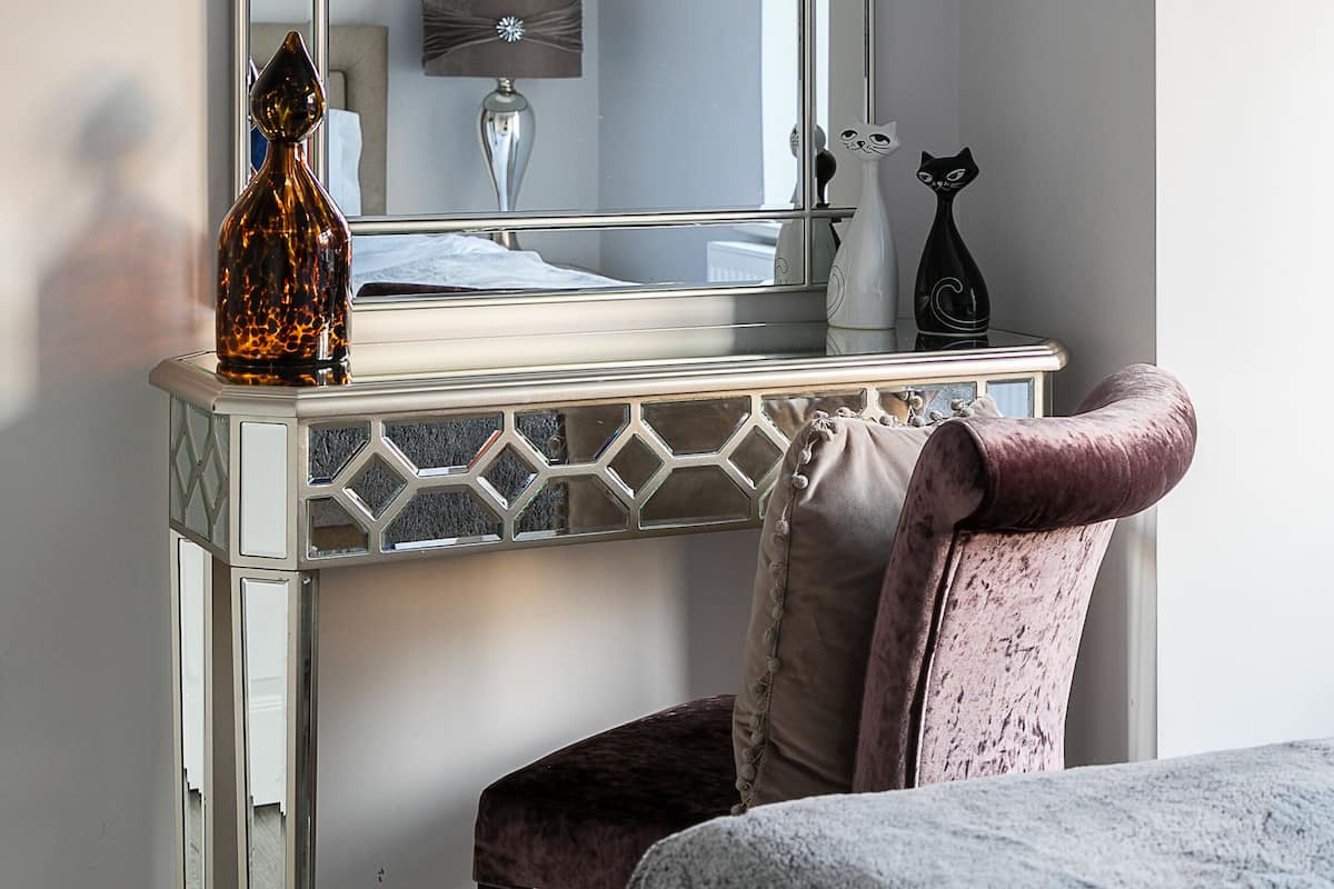 Une chambre à coucher comprenant une coiffeuse, un miroir, un lit et un coussin décoratif.