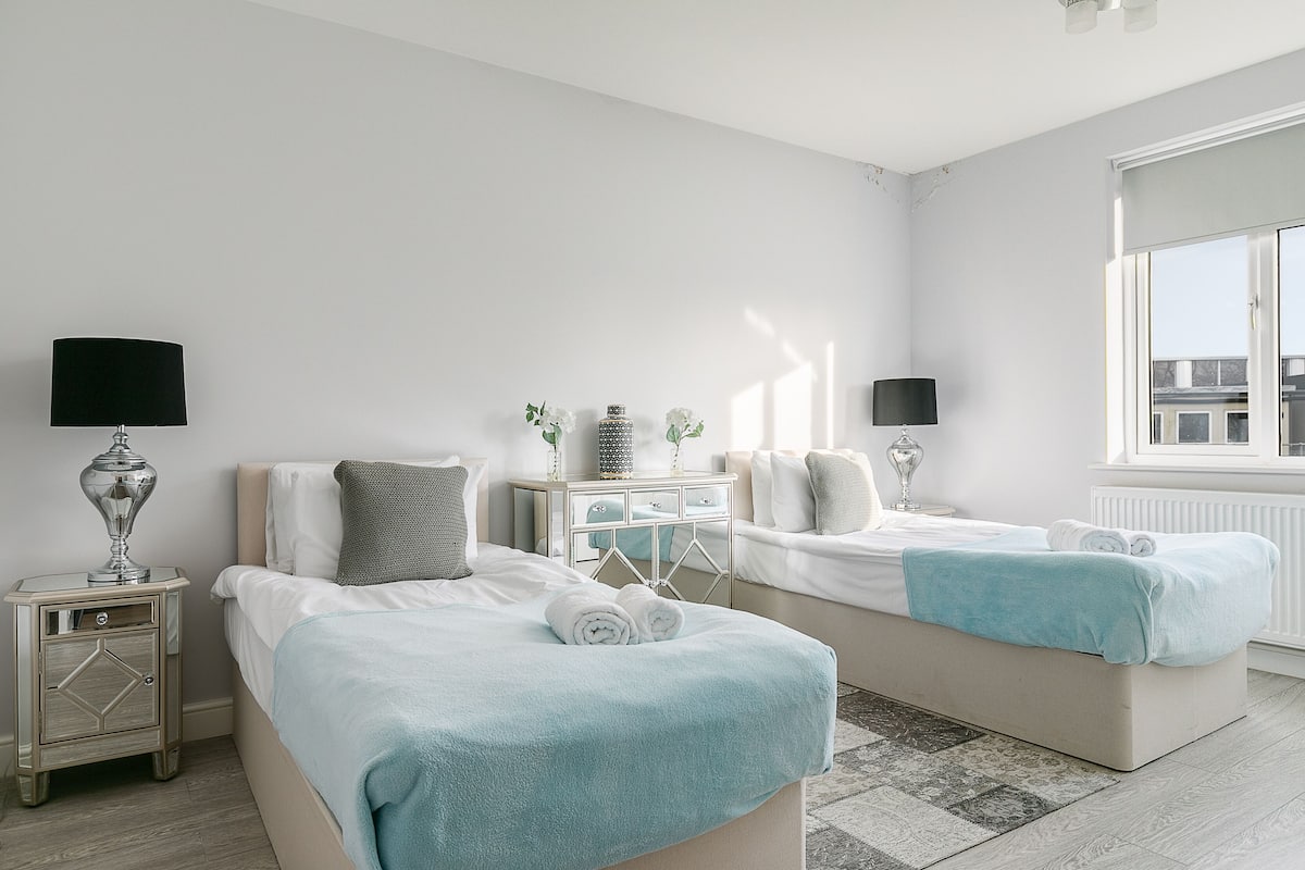 Une chambre moderne avec deux lits, une table de chevet, une commode et une fenêtre donnant sur un beau paysage.