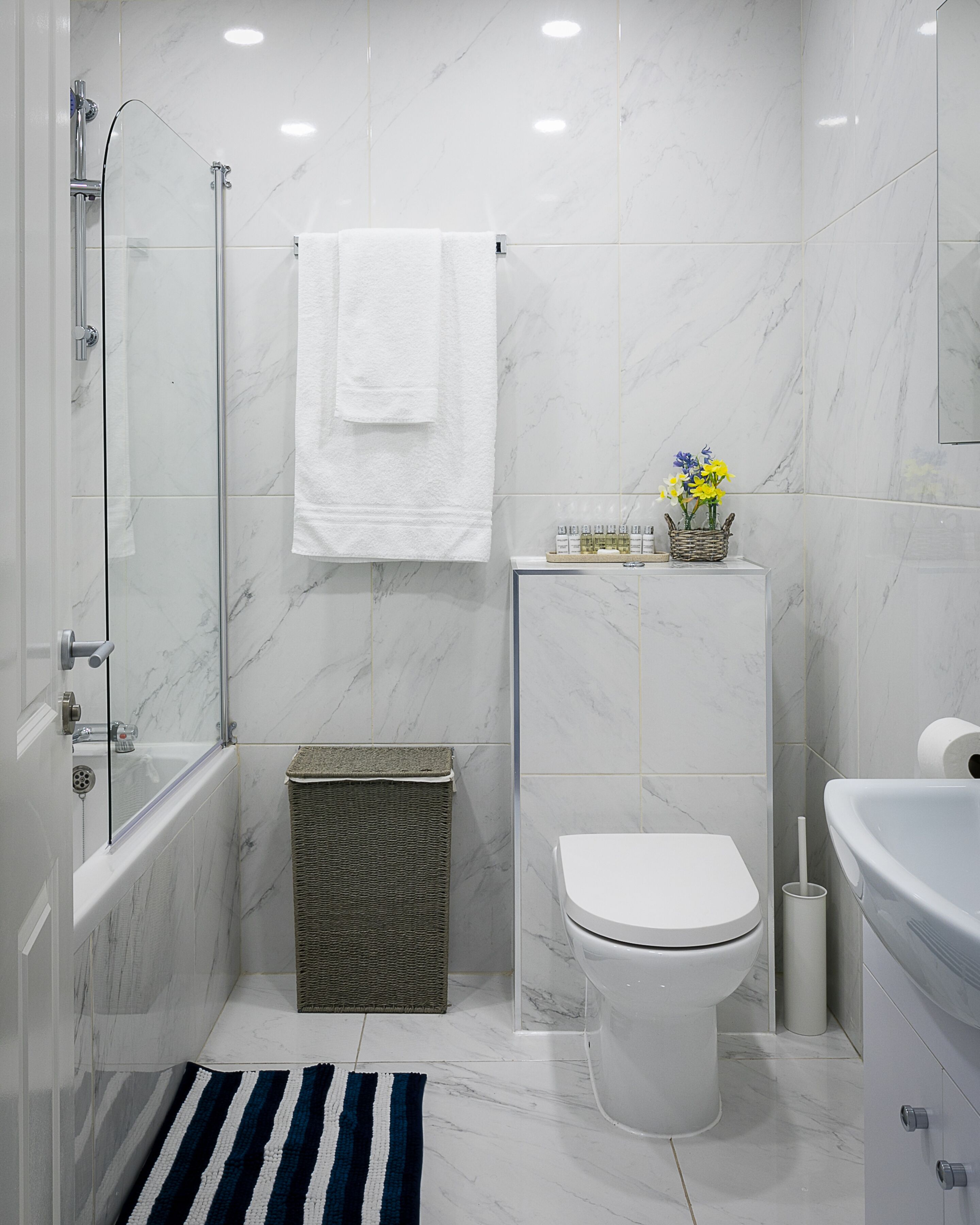 Une salle de bain moderne avec une douche à parois de verre, des toilettes blanches, une baignoire et un petit panier en osier.