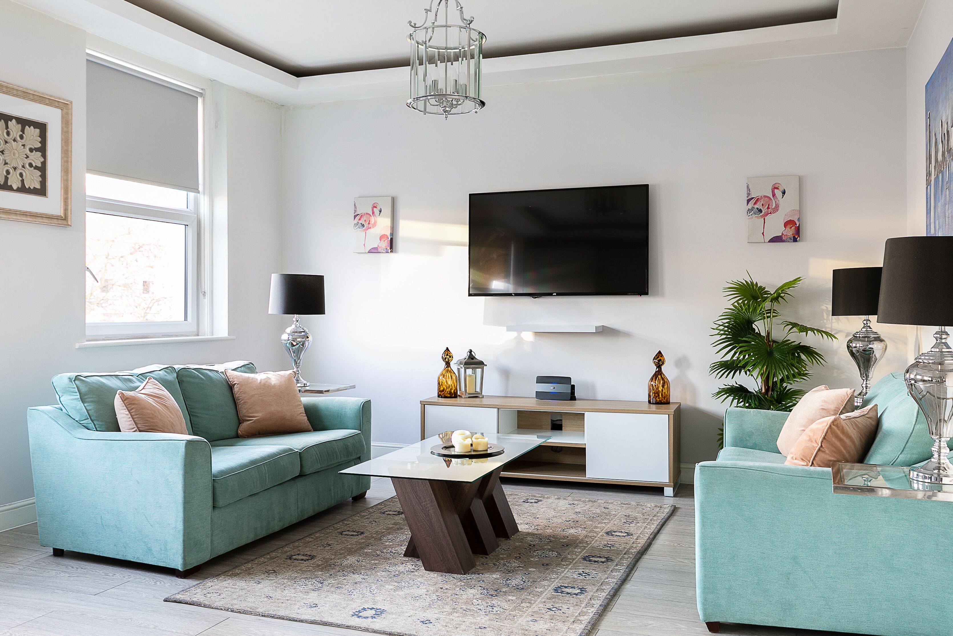 A modern living room with teal sofas, a flat-screen TV, and decorative items.